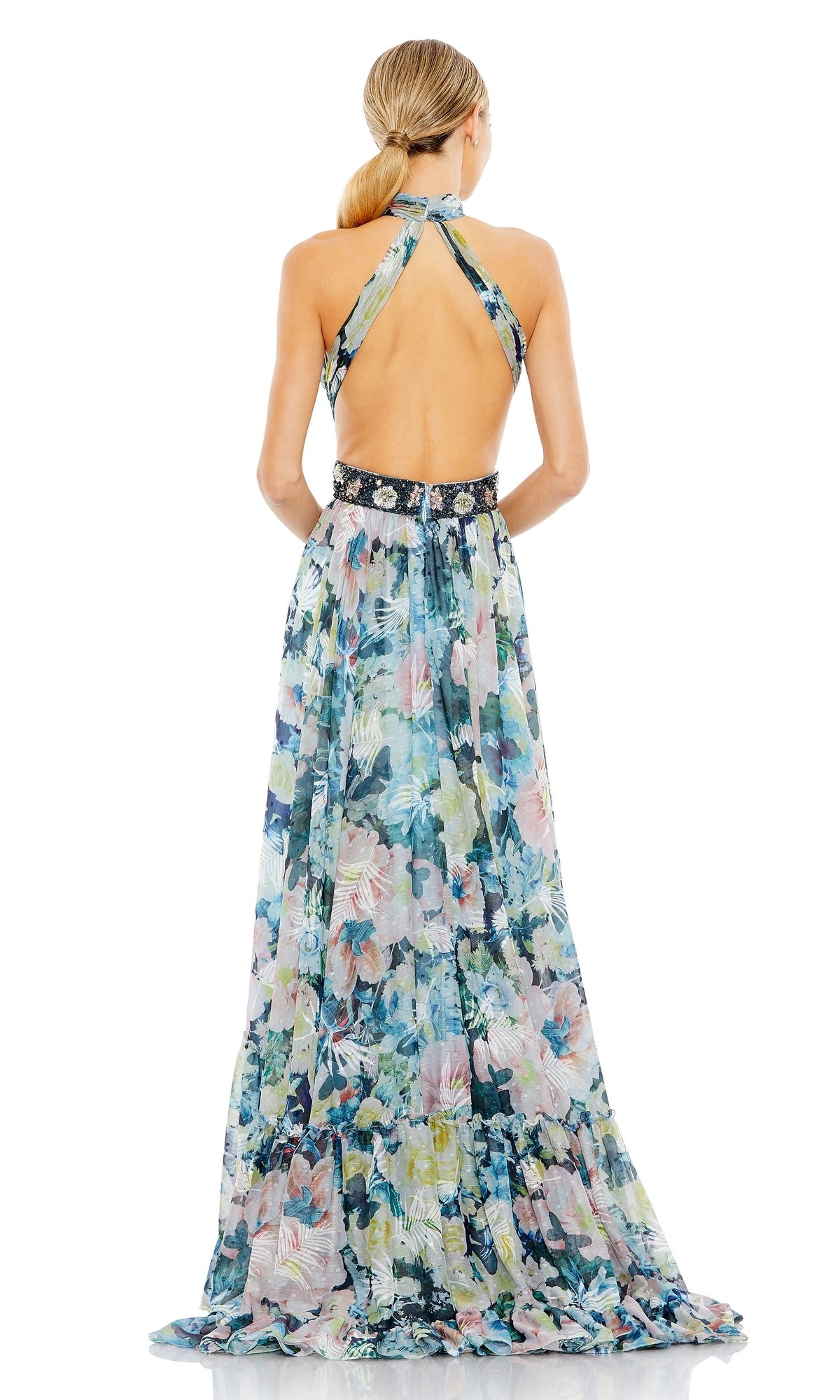 A woman stands facing away, wearing the Mac Duggal Long Formal Dress 68089—a sleeveless, floor-length pastel floral gown with an open back and black waistband.
